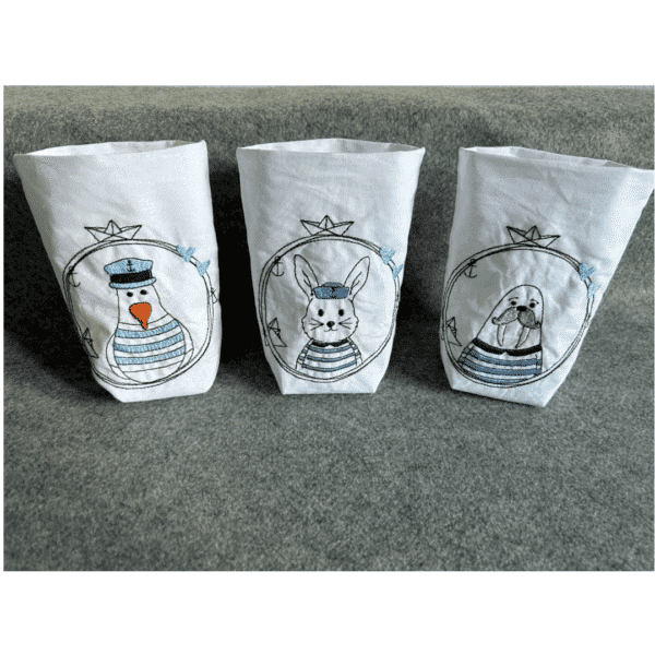 Drei bestickte Stofftaschen mit Tiermotiven. Von links nach rechts: ein Pinguin mit Mütze, ein Hase mit Mütze und ein Walross mit gestreiftem Pulli, jeweils in blau-weißen Tönen.