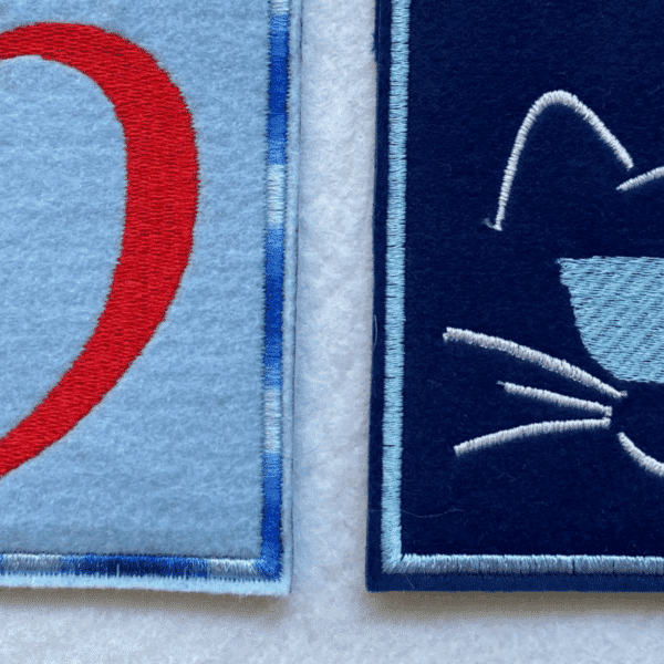 Impfausweishülle aus Filz für Katzen: Detailaufnahme von Filzhüllen mit einem Rand in einfarbig und mehrfarbig und gestickten Katzenmotiven.