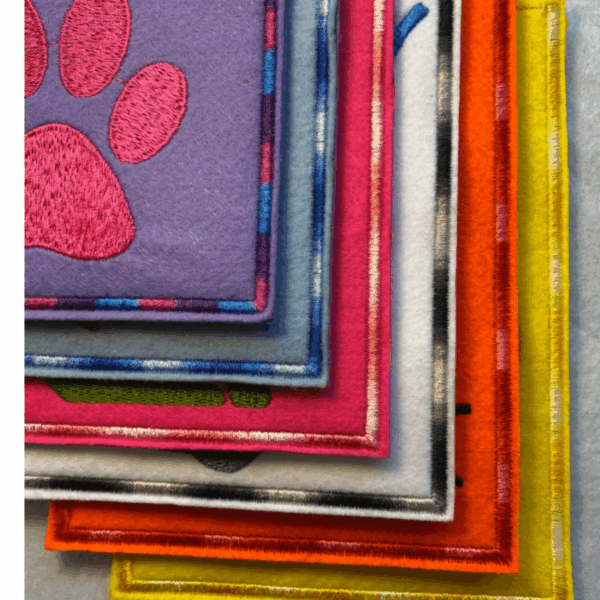 Impfausweishülle aus Filz für Katzen: Nahaufnahme der mehrfarbigen Ränder verschiedener Filz-Impfausweishüllen mit Namen und Motiven.