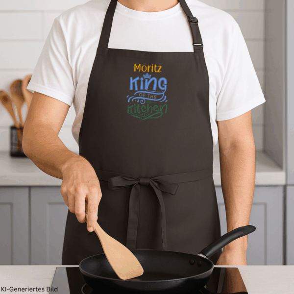 Mann in weißem Shirt trägt eine schwarze personalisierte Kochschürze mit dem Text „Moritz – King of the Kitchen“.