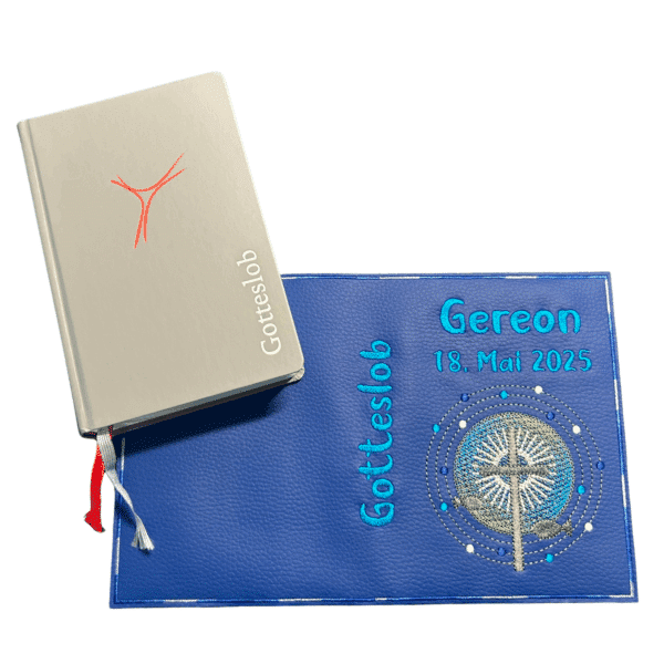 Bestickte Gotteslobhülle aus Kunstleder in Blau, aufgeklappt neben einem Gotteslob – personalisiert mit Name und Datum