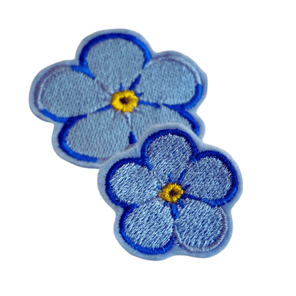 Zweier-Set des Forget Me Not Ansteckers in mehrfarbigem blau mit gelber Mitte, gestickt. In zwei Größen zu sehen.