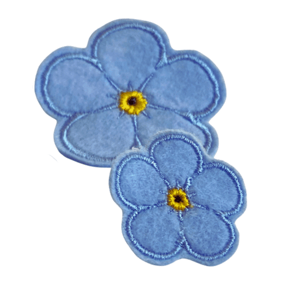Zweier-Set des Forget Me Not Ansteckers in einfarbig hellblau, gestickt, in zwei Größen, auf weißem Hintergrund.