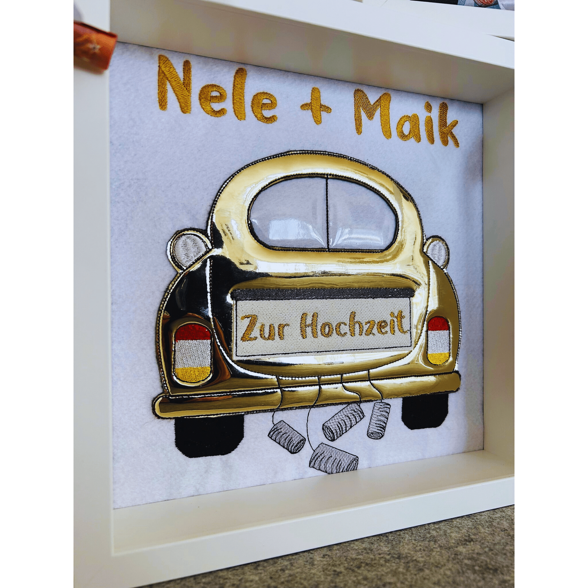 Geldgeschenk zur Hochzeit mit goldfarbenem Auto und Namen Nele & Maik in einem Bilderrahmen, dekoriert mit Dosen und Geldrollen.