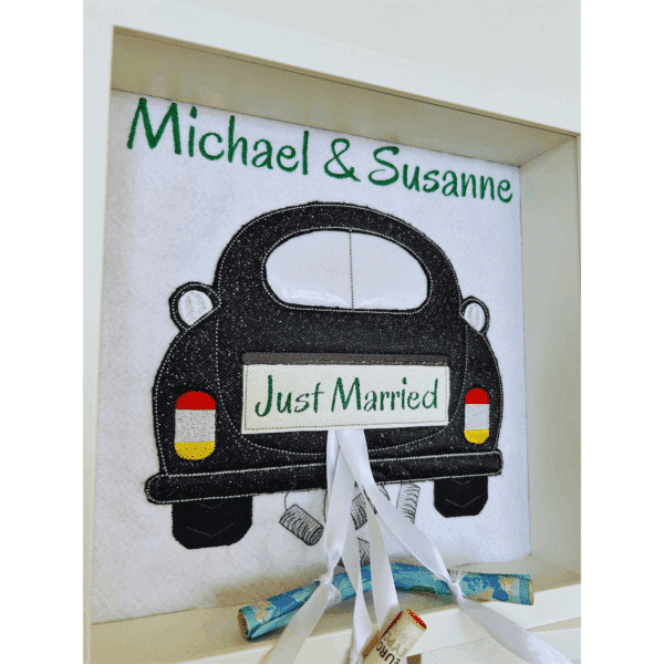 Geldgeschenk zur Hochzeit in Bilderrahmen mit schwarzem Auto, personalisiert mit Michael & Susanne und verziert mit Geldscheinen.
