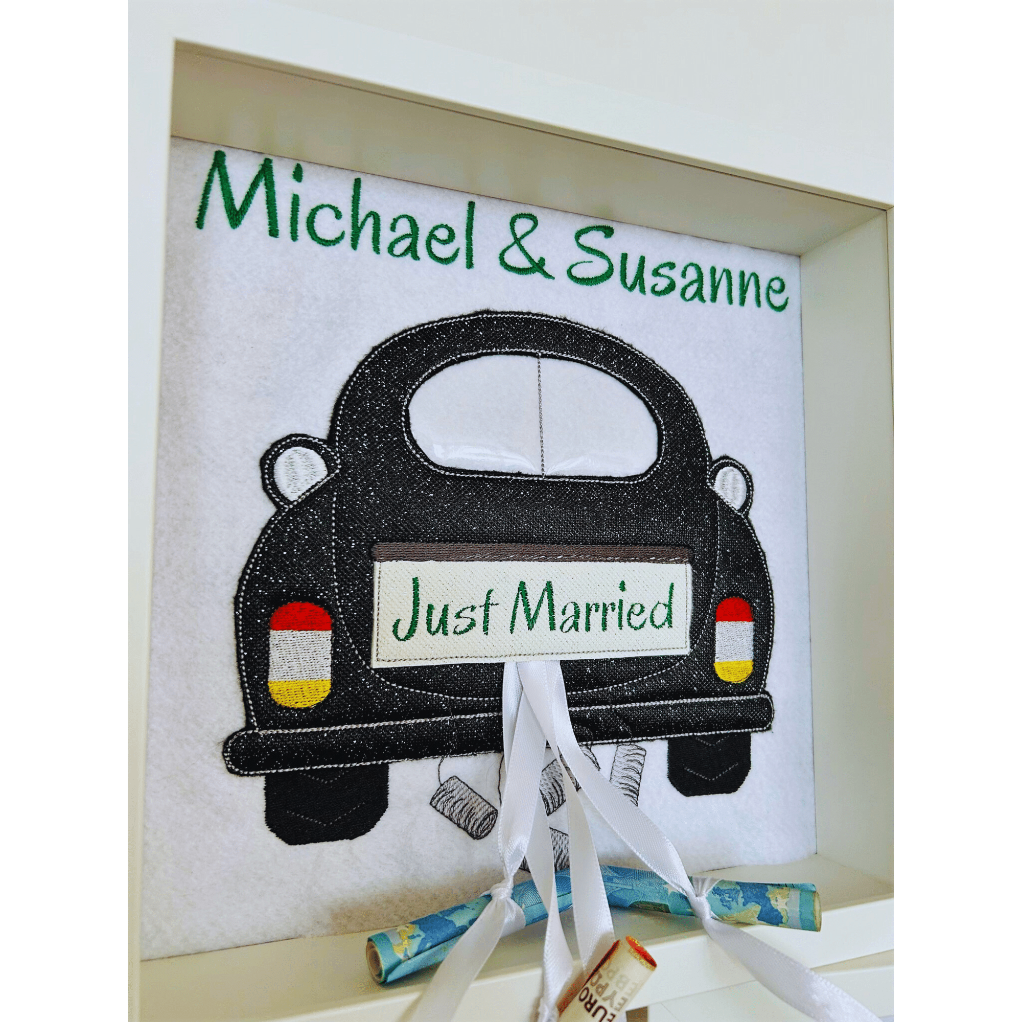 Geldgeschenk zur Hochzeit in Bilderrahmen mit schwarzem Auto, personalisiert mit Michael & Susanne und verziert mit Geldscheinen.