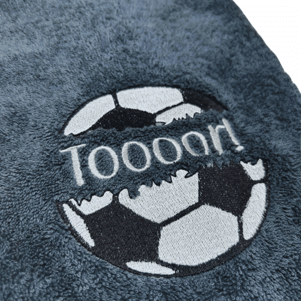 Fußballhandtuch mit Split-Motiv und Name: Nahaufnahme der Stickerei mit Fußball und Schriftzug Toooor auf grauem Handtuch