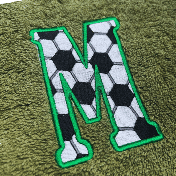 Fußballhandtuch mit Zahl oder Buchstabe: Detailaufnahme der Stickerei Buchstabe M im Fußballmuster auf grünem Handtuch